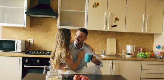 Uśmiechnięta para pije kawę w przytulnej, nowoczesnej kuchni
