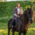 Kobieta jedzie na czarnym koniu przez zieloną łąkę w słoneczny dzień