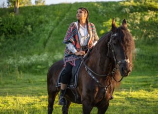 Kobieta jedzie na czarnym koniu przez zieloną łąkę w słoneczny dzień